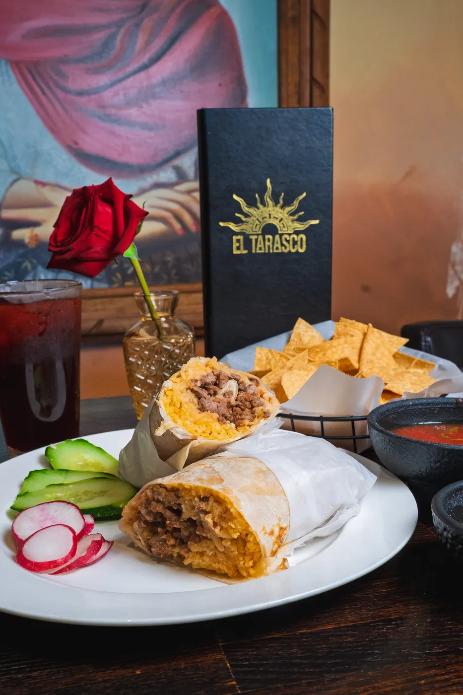 A grilled burrito plated with radish and cucumber next to fresh salsa